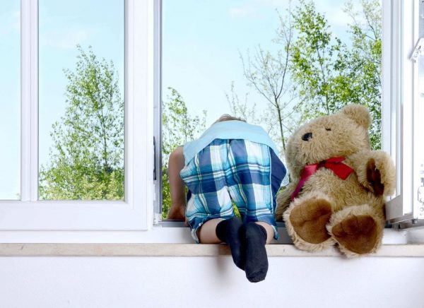 child with teddybear looking outside window